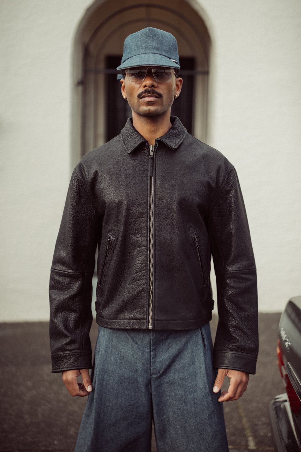 Edd model wearing a black leather jacket and blue cap outside.