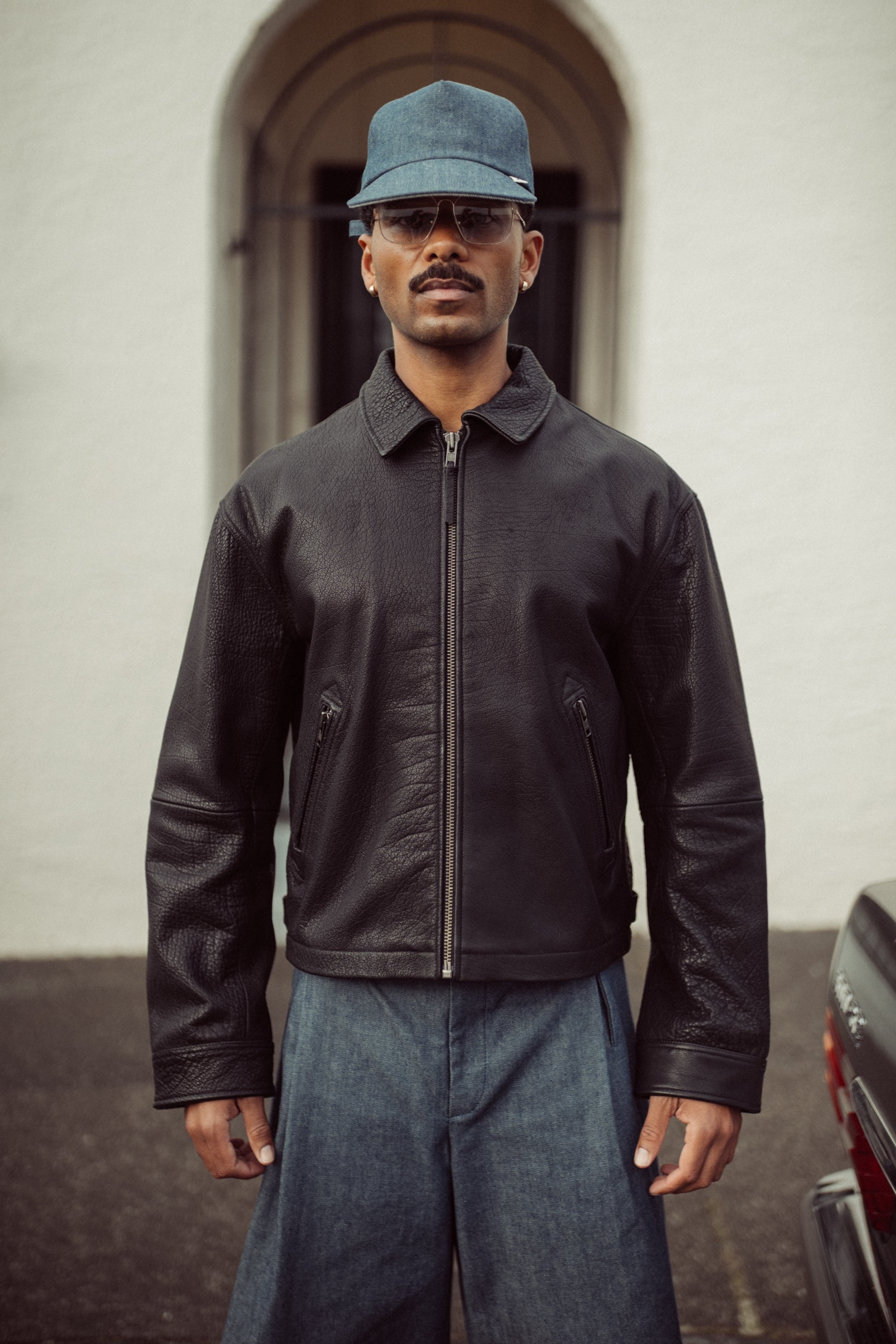 Edd model wearing a black leather jacket and blue cap outside.