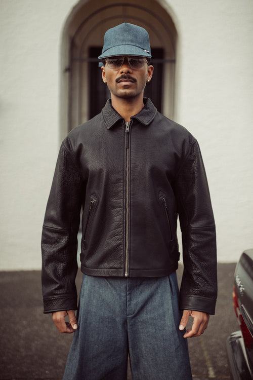 Edd model wearing a black leather jacket and blue cap outside.